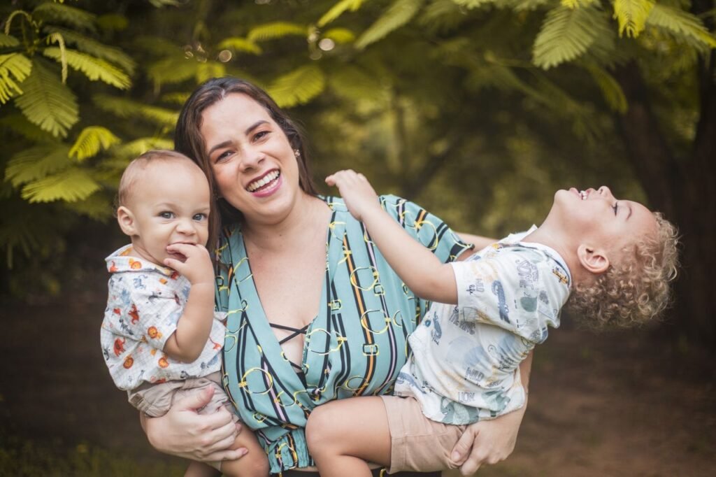 A mother joyfully holds her two children in a vibrant green park, enjoying a summer day together.